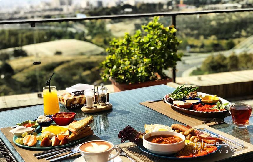 میز صبحانه‌ای در یک کافی‌شاپ که سه ظرف غذا روی میز و منظره‌ای فلو از شهر در ارتفاع در جلوی تصویر دیده می‌شود. 